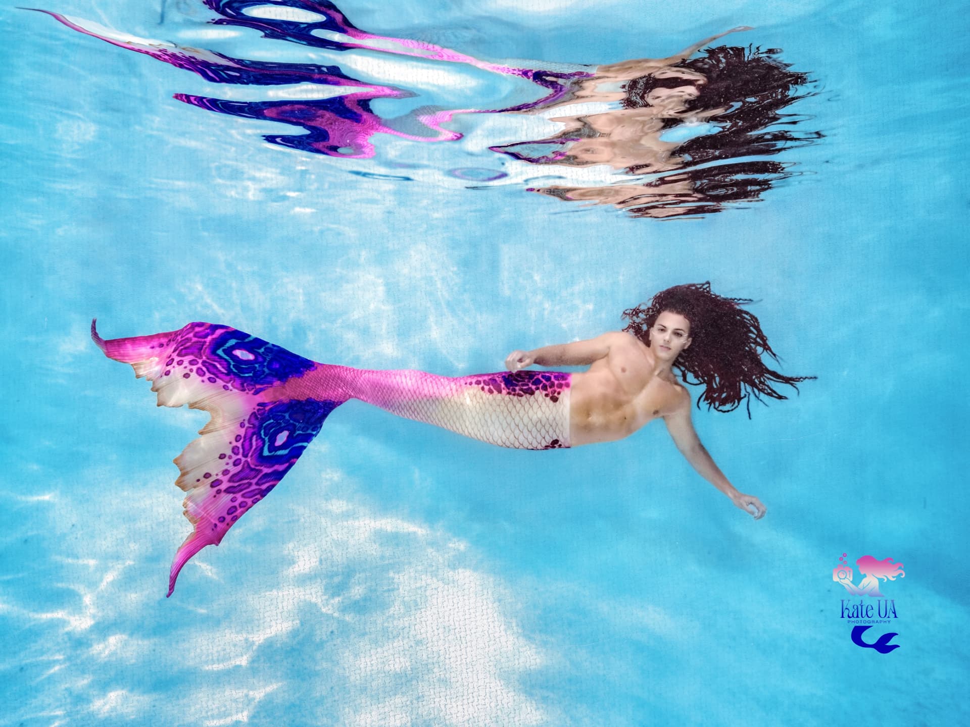 Prince Pōhaku gliding just beneath the surface of a sunlit pool, magenta and violet tail fin spread wide