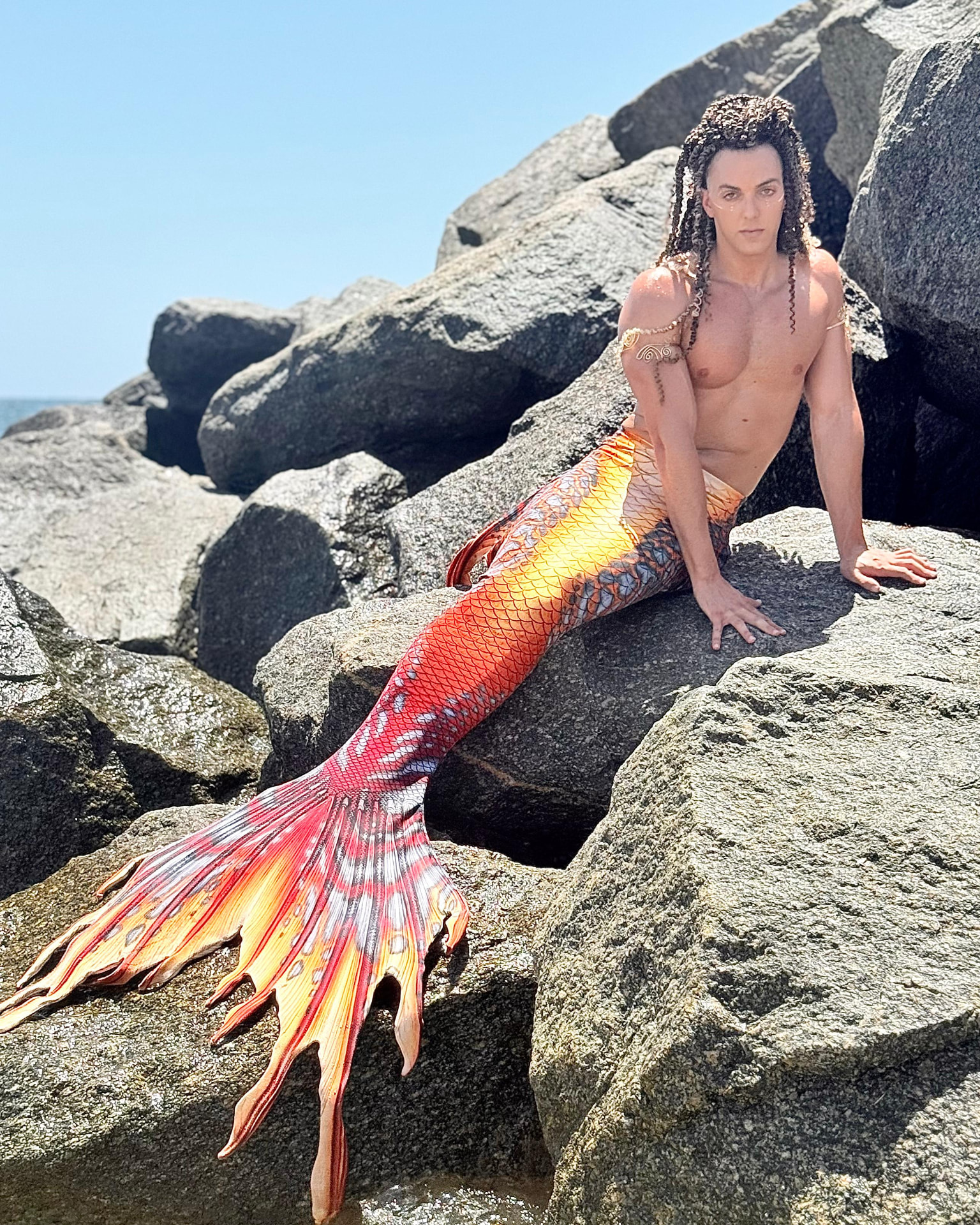 Prince Pōhaku seated on coastal boulders, fiery tail stretching across the rocks